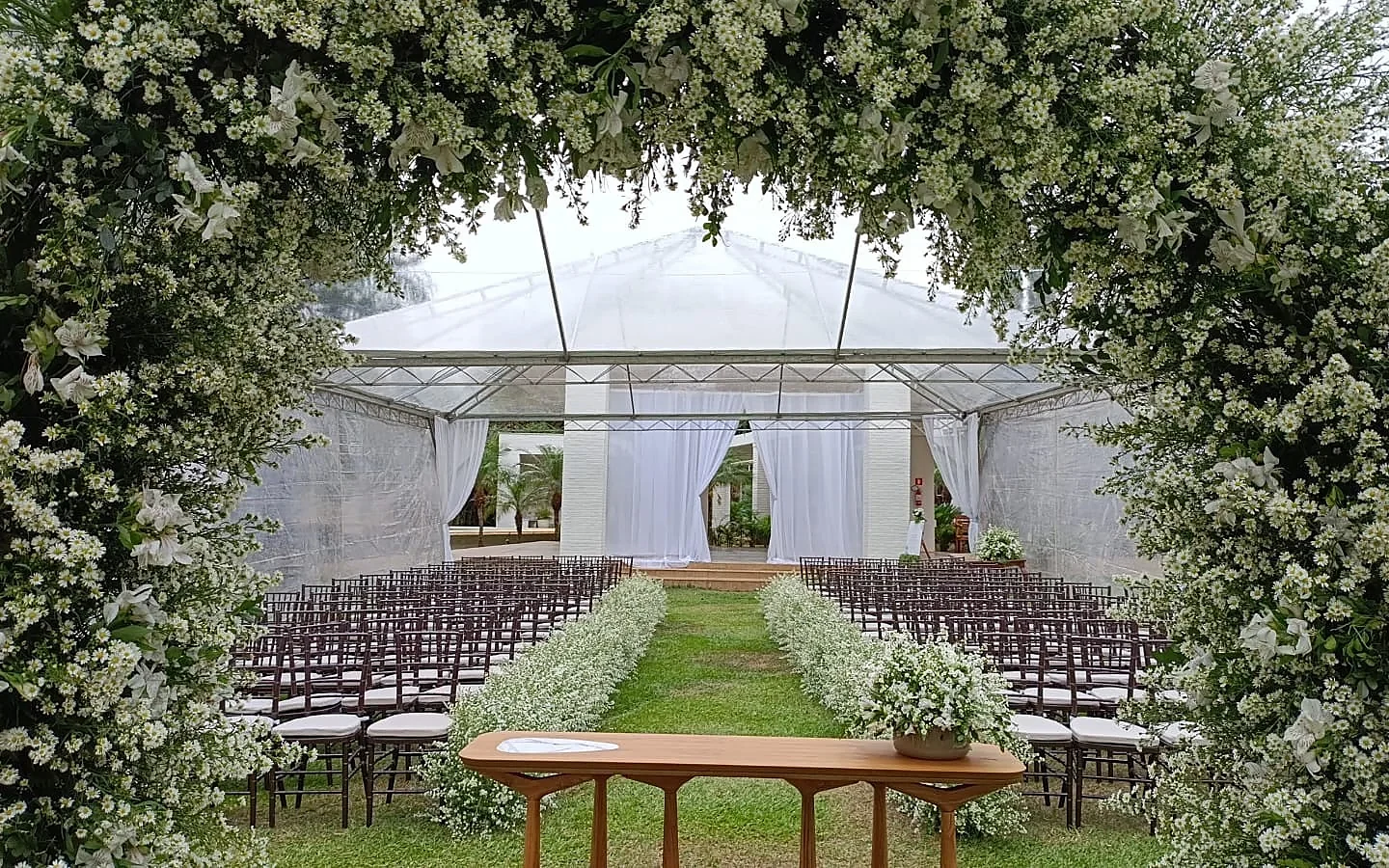 Cerimônia de casamento sob tenda cristal com arco de flores